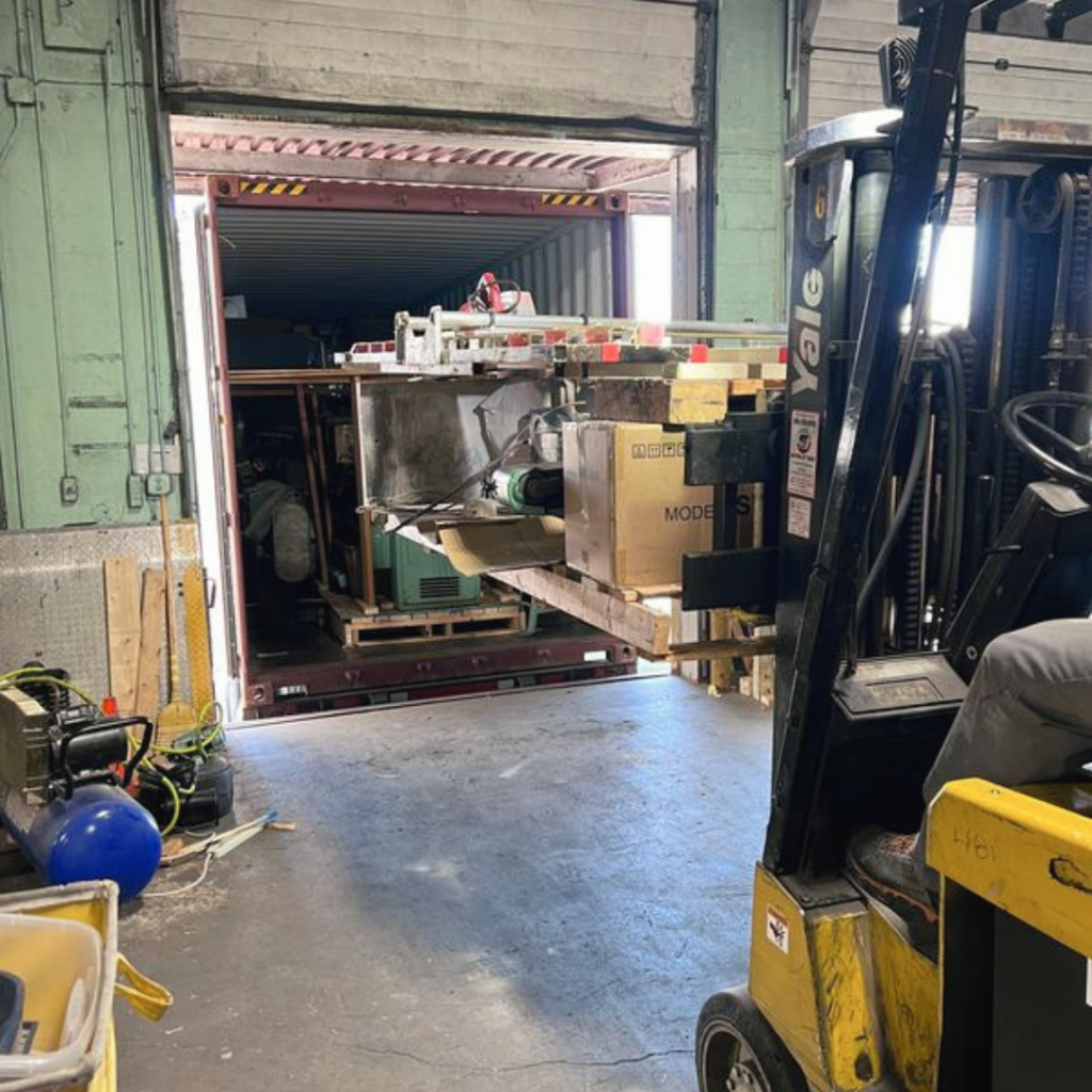 Forklift loading surplus industrial equipment into a shipping container for liquidation and resale 